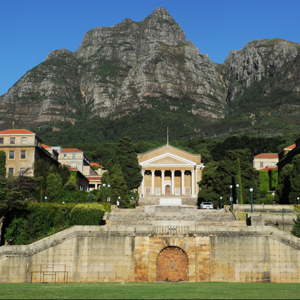 UCT buildings in front of a mountain with two people walking a a white BMW