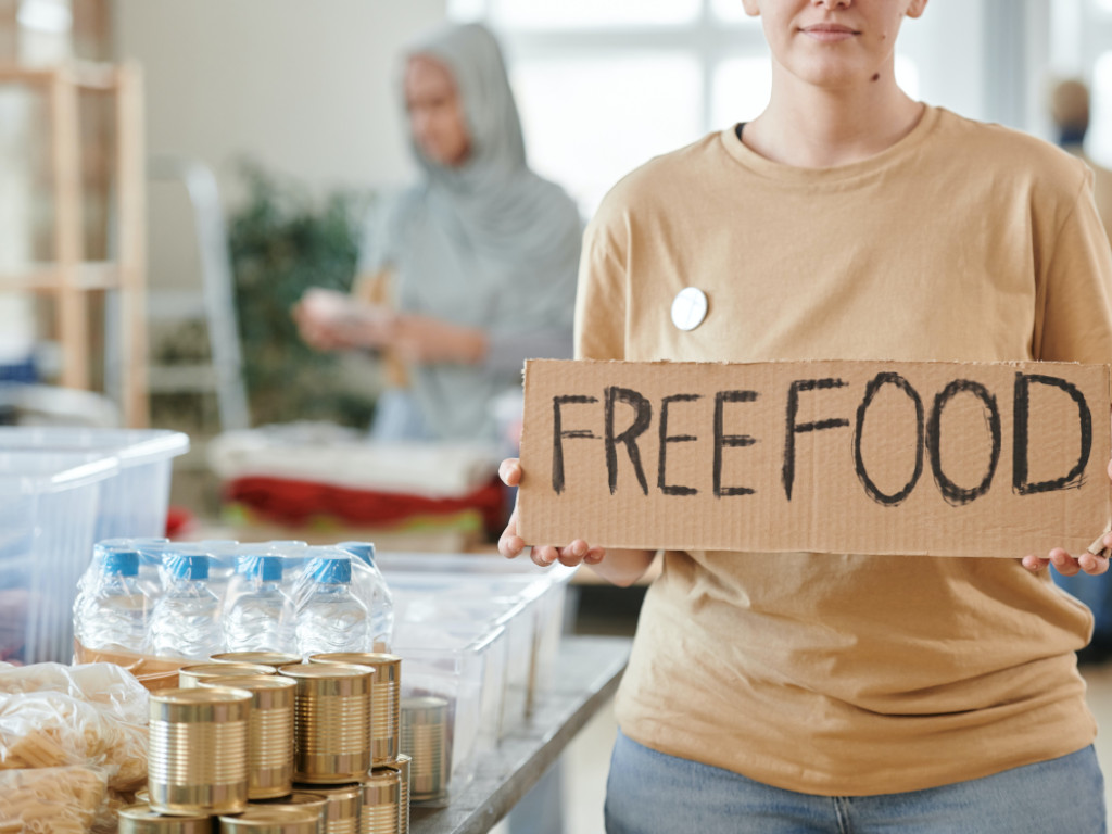 woman standing next to cans and water bottles holding a free food sign